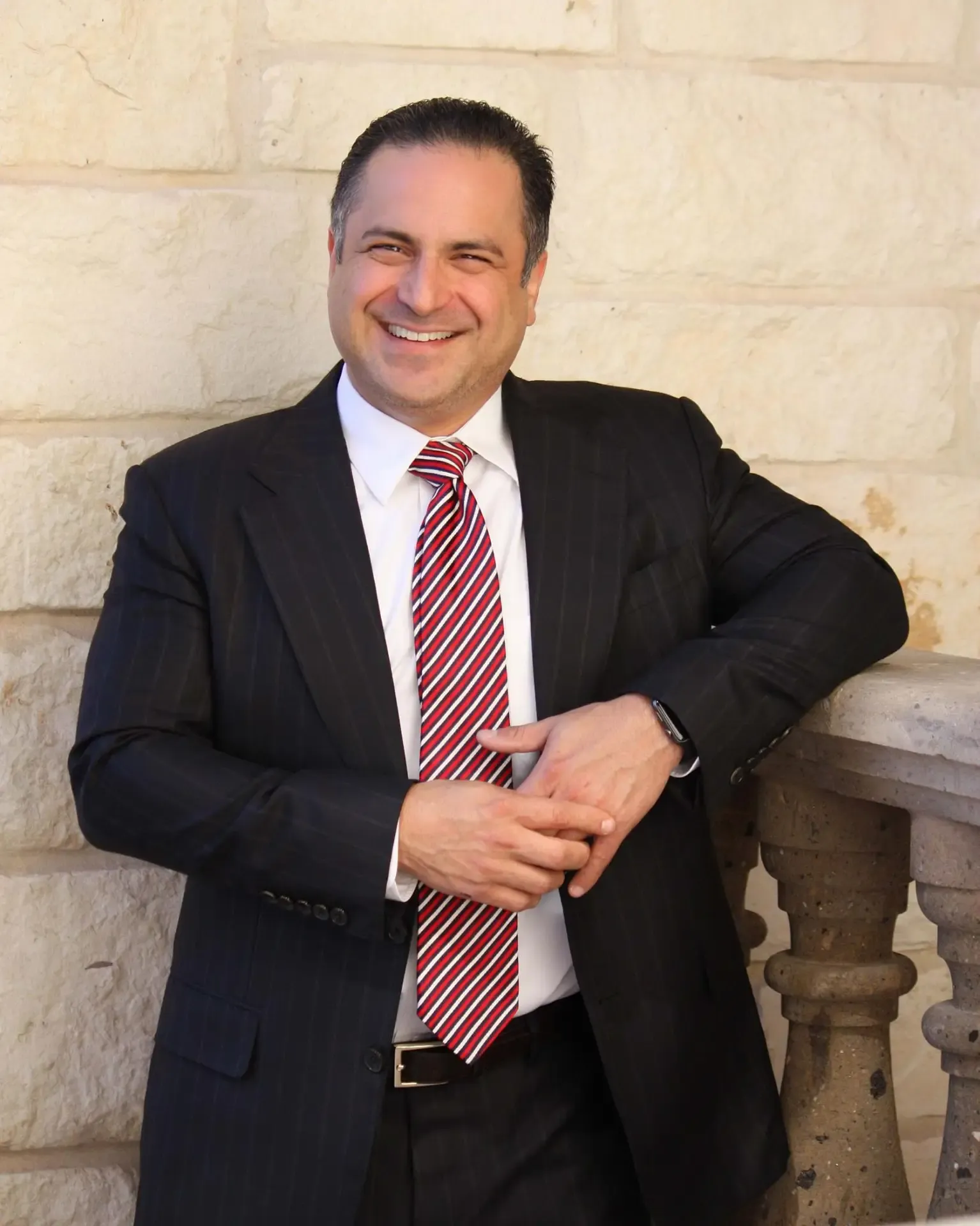 Joseph J. Raetzer, MBA, JD, in a dark suit and striped tie standing against a stone wall